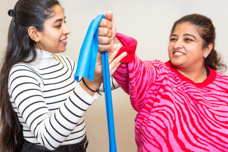 A female physiotherapist demonstrating use of a tension band to a female patient