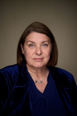 Headshot of Caroline Hallett, a woman against a pale background in a blue top.