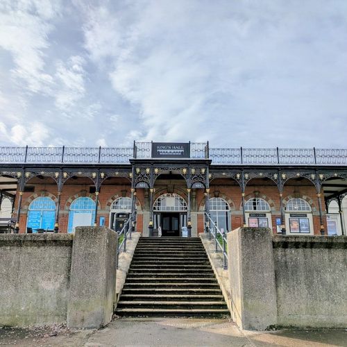 Front elevation of King’s Hall in Herne Bay, a brick historic building with a central staircase leading to arched entrance doors beneath a decorative iron canopy