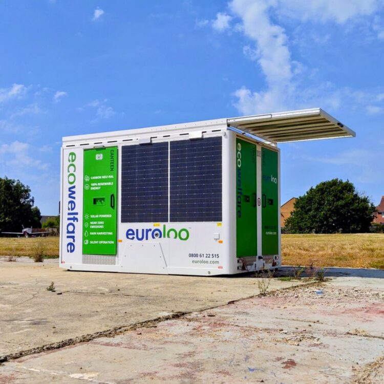Portable solar-powered euroloo ecowelfare cabin equipped with rooftop solar panels, situated on a remote site under a clear blue sky.