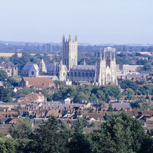 Distant view of Canterbury Cathedral rising above the surrounding cityscape, with trees and residential buildings in the foreground